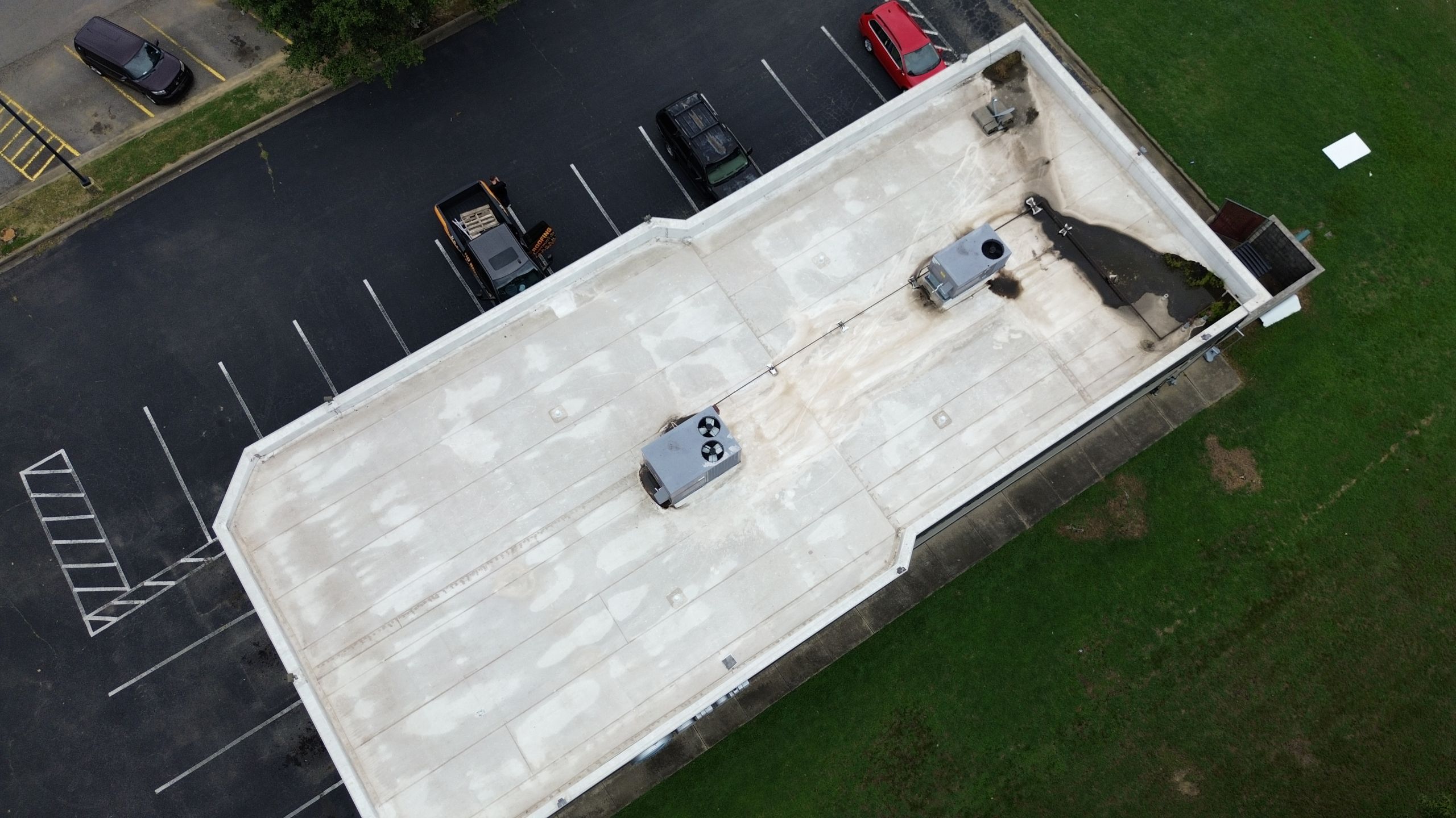 Aerial view of a flat-roofed building with HVAC units, referred as a commercial roof maintenance. Cars are parked in the adjacent lot.