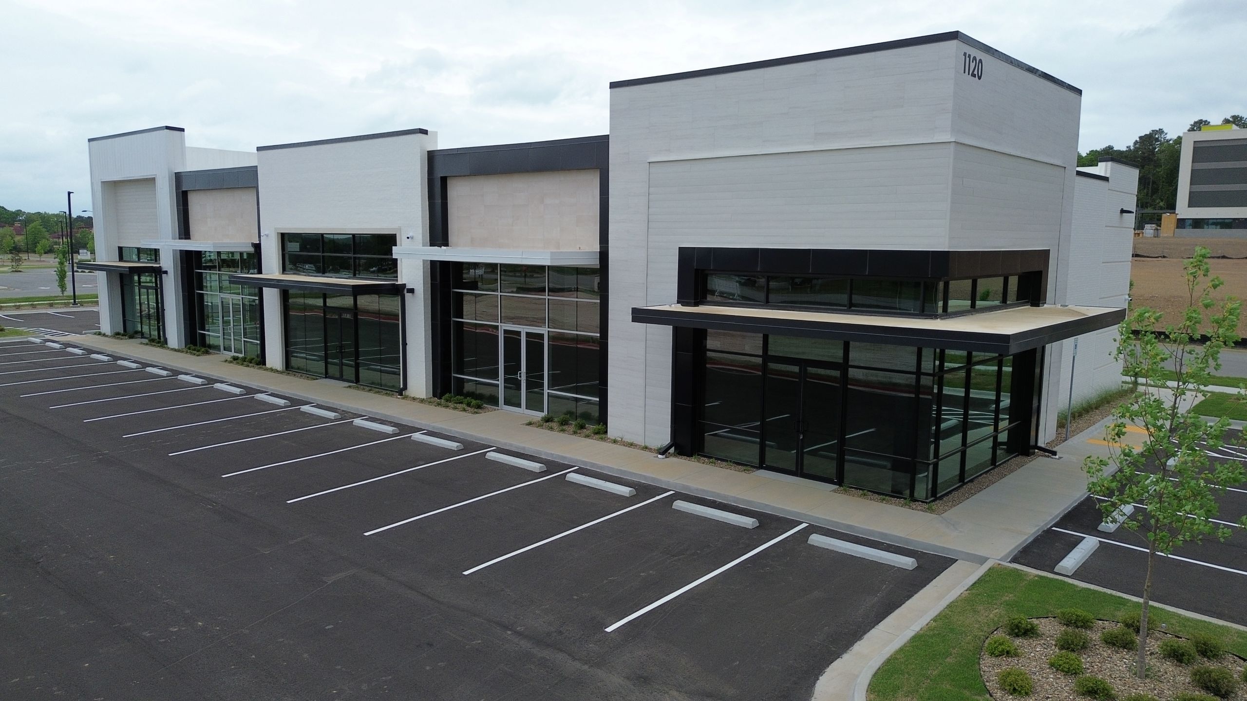 A modern, empty commercial building with large glass windows and a vacant parking lot. The building is white with black accents and surrounded by minimal landscaping.