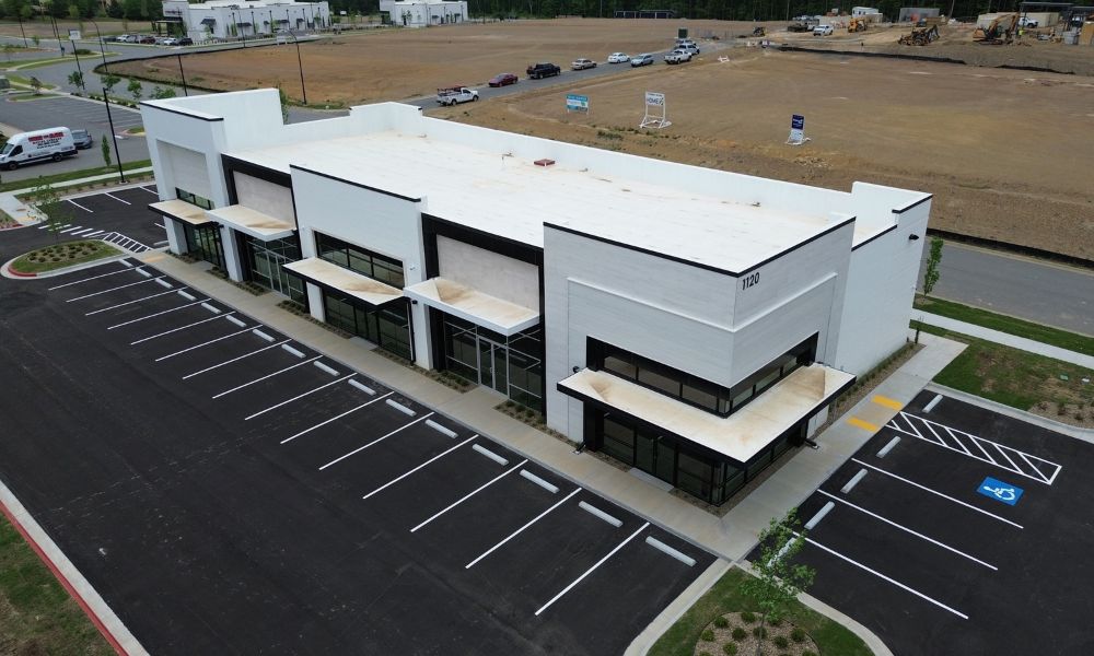Commerical - Multi-Tenant Aerial view of a modern white commercial building with black trim and the number 1120 displayed on the corner, surrounded by a paved parking lot often serviced by an Arkansas roofing company.